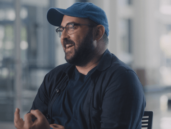 Man wearing baseball cap and glasses talking and gesticulating
